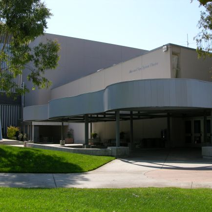 A large, imposing building with a modern architectural design, surrounded by greenery and clear blue skies.