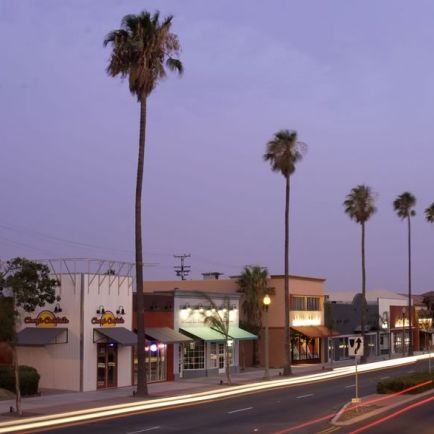 A serene street lined with palm trees and shops, illuminated by the soft glow of dusk.
