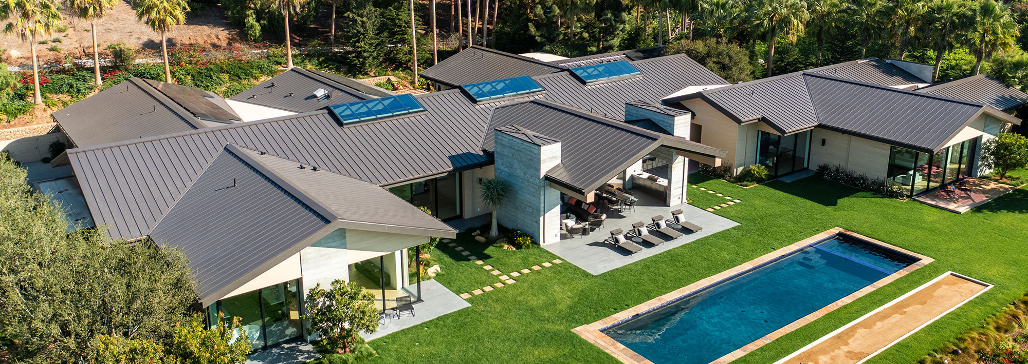 Aerial view of a residential property featuring a swimming pool surrounded by greenery and outdoor seating areas.