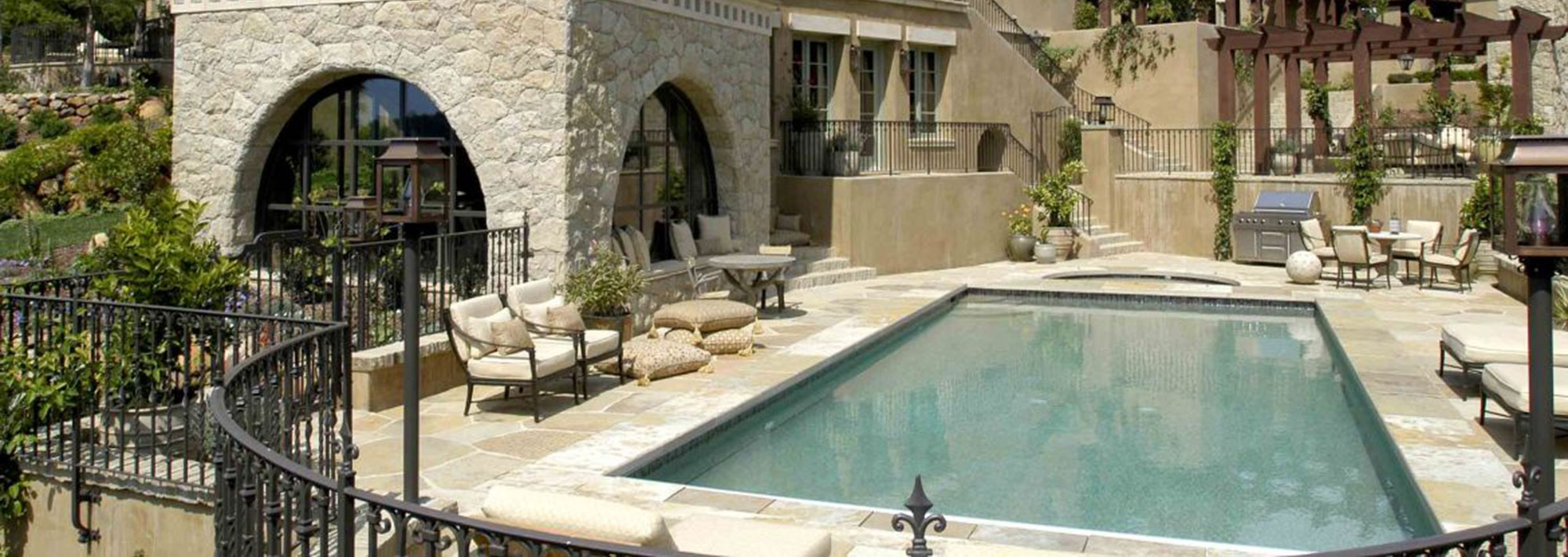 A serene home pool surrounded by a stone wall and elegant patio furniture, inviting relaxation and leisure.